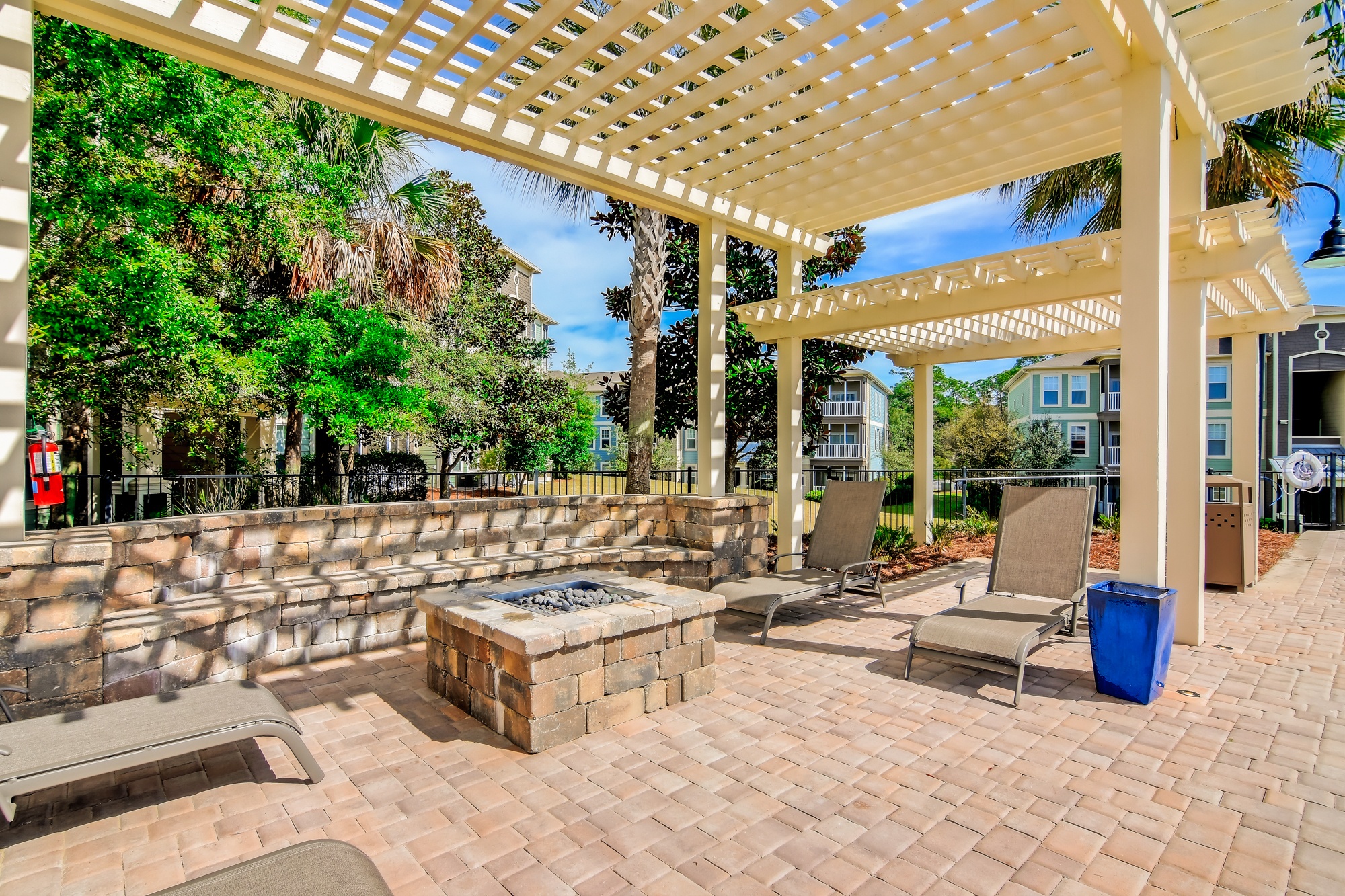 A patio with a fire pit and chairs under a pergola.